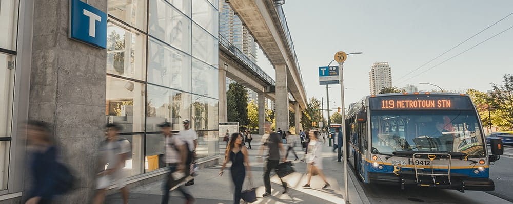 A bus at a bus stop in front of a SkyTrain station