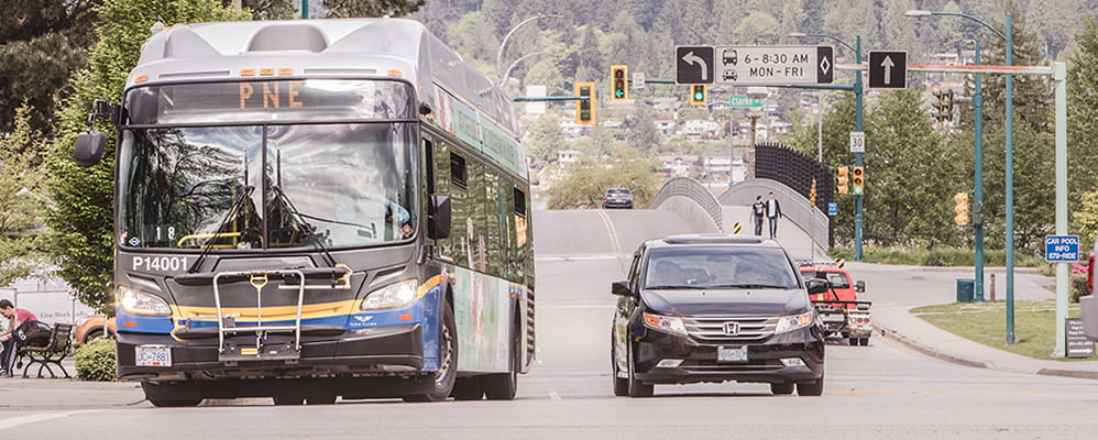 A bus driving next to a black car on an empty street with trees in the background